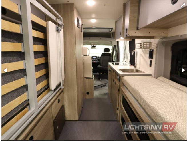 RV rental interior: a compact camper van layout with a galley kitchen, fold-up bed, and convertible seating.