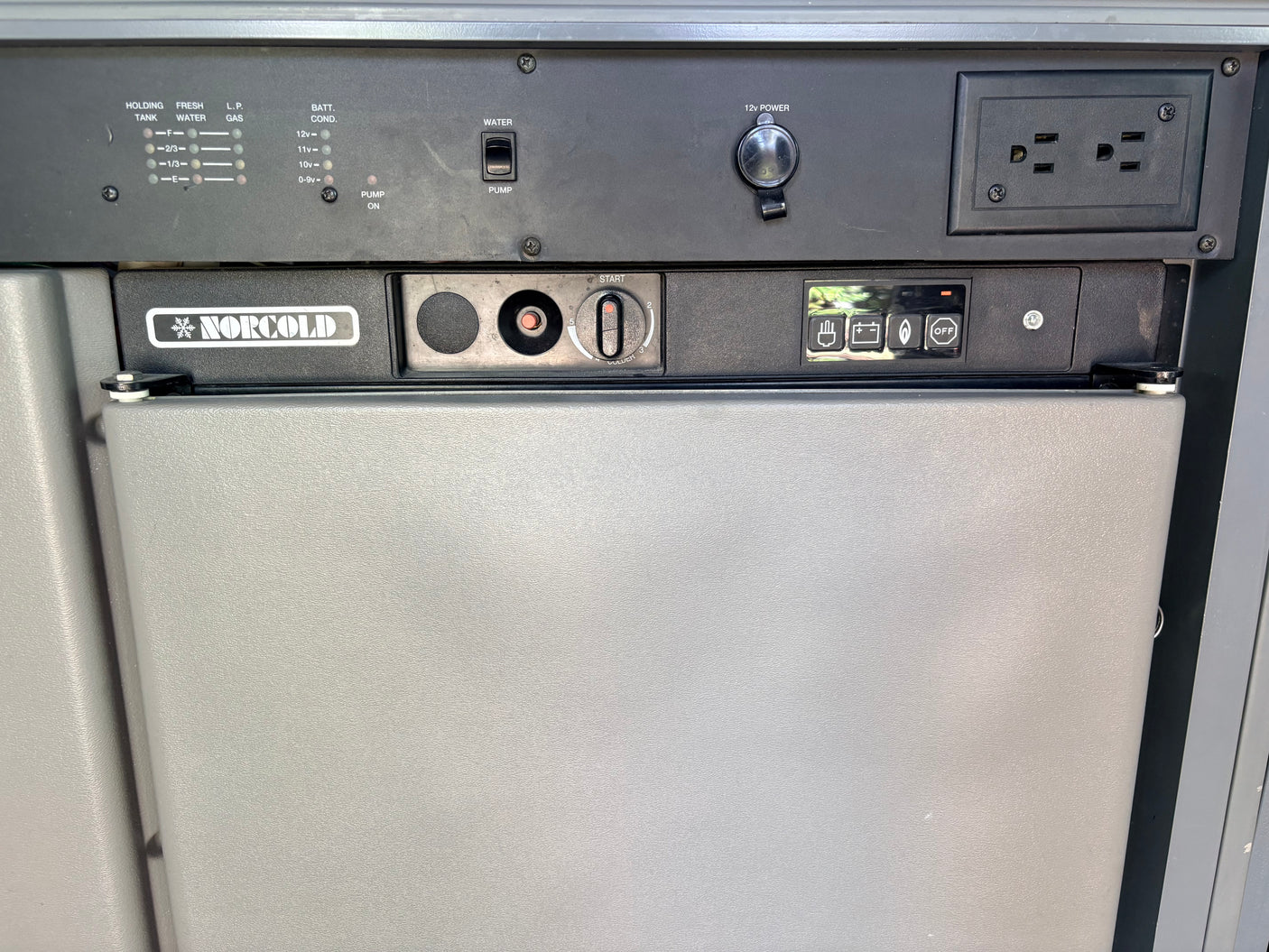 RV rental interior: Detailed view of a Norcold refrigerator and control panel with tank levels, battery status, water pump, 12V/AC outlets.