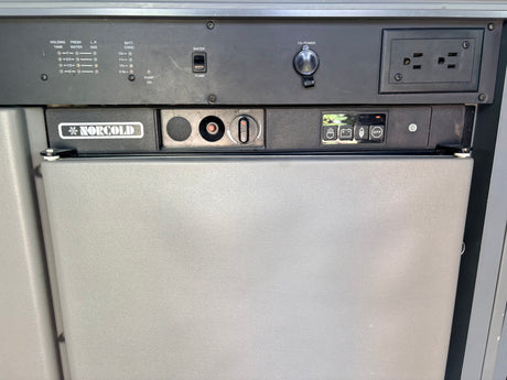 RV rental interior: Detailed view of a Norcold refrigerator and control panel with tank levels, battery status, water pump, 12V/AC outlets.