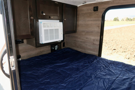 Inside an RV rental: a cozy bedroom with dark wood cabinets, a window AC unit, and a blue bed, ready for adventure.