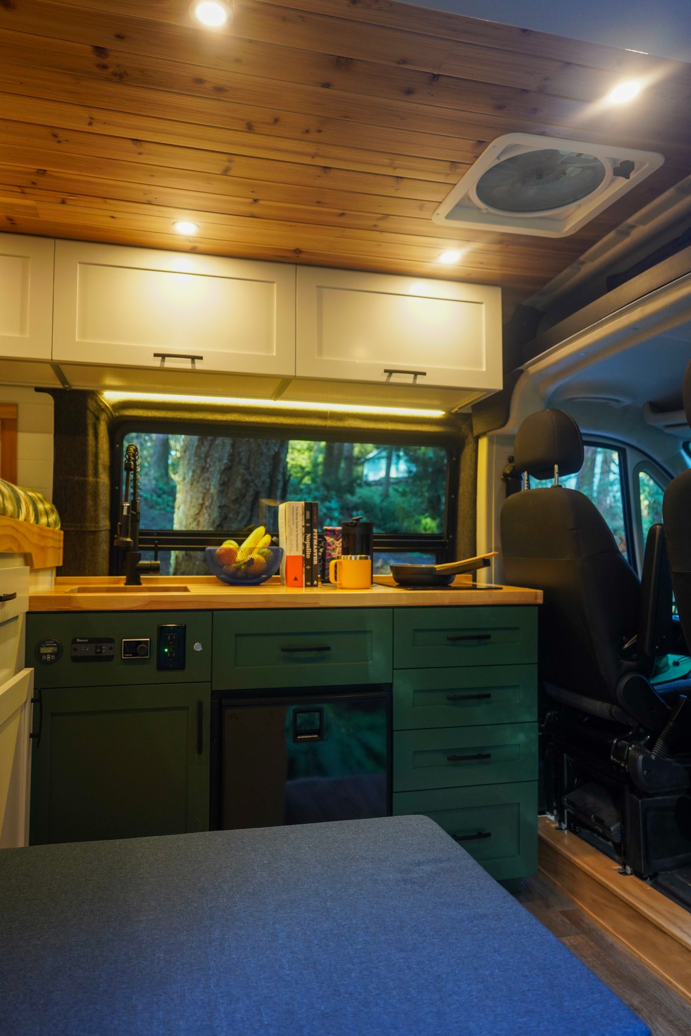 This rv rental features a cozy interior with a modern green kitchen, wood ceiling, and built-in amenities for travel.
