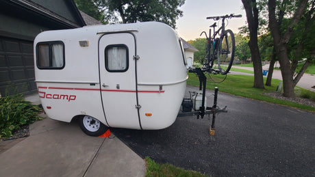 Compact Scamp travel trailer, ideal for an RV rental, parked on a driveway with a bike rack for camping adventures.