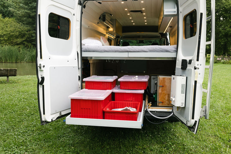 RV rental camper van interior: rear doors reveal a bed, pull-out storage with red bins, and external water heater. — photo 8