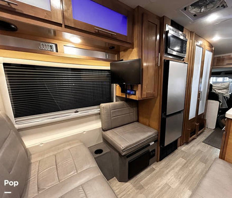 RV rental interior features comfortable seating, window blinds, TV, microwave, and fridge within light wood cabinetry, ideal for travel.