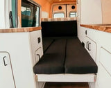 Inside this RV rental camper van, a dark grey folding bed is flanked by white cabinets with wood countertops.