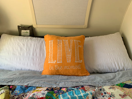 Cozy RV rental bed with "LIVE in the moment" pillow and patchwork quilt, ideal for comfortable travel.