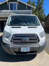Front view of a white Ford Transit van, a potential RV rental, parked in a driveway. Oregon plate: 190 RBY.