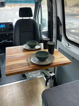 Compact dining setup in an RV rental camper van, featuring an adjustable wooden table with two place settings and cups for mobile living.