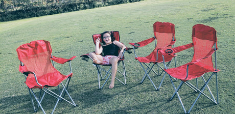 Perfect RV rental getaway! A young girl smiles in a red camp chair, with three more chairs on green grass.