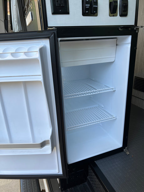 RV rental mini-fridge is open, revealing empty shelves and door storage. Ideal for road trips.