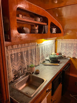 A well-appointed rv rental kitchen featuring rich wood cabinetry, a sink, microwave, induction cooktop, and lace curtains.