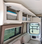 Interior of an RV rental showing open overhead cabinets with storage baskets, comfortable seating, and a window view.