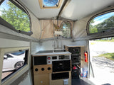 RV rental interior: compact kitchen, organized crate storage, and pop-top windows with outdoor views.