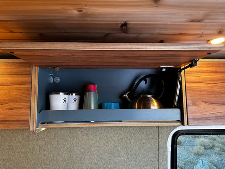 Organized RV rental kitchen cabinet: open, with a shiny kettle, white cups, and colorful bowls, ready for travel or camping.