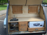 Rear kitchen galley of an RV rental: features a sink, faucet, cooler on a pull-out drawer, and wooden storage.