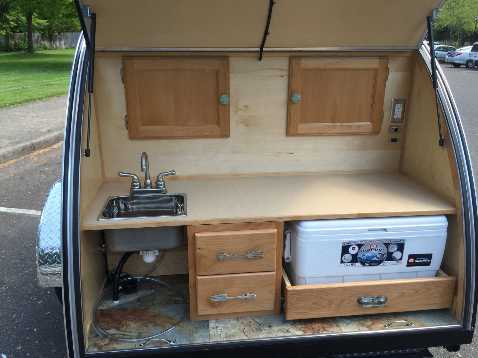 Rear kitchen galley of an RV rental: features a sink, faucet, cooler on a pull-out drawer, and wooden storage.