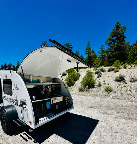 Luna Rover teardrop RV rental, with its open outdoor kitchen, parked in a sunny, natural setting.