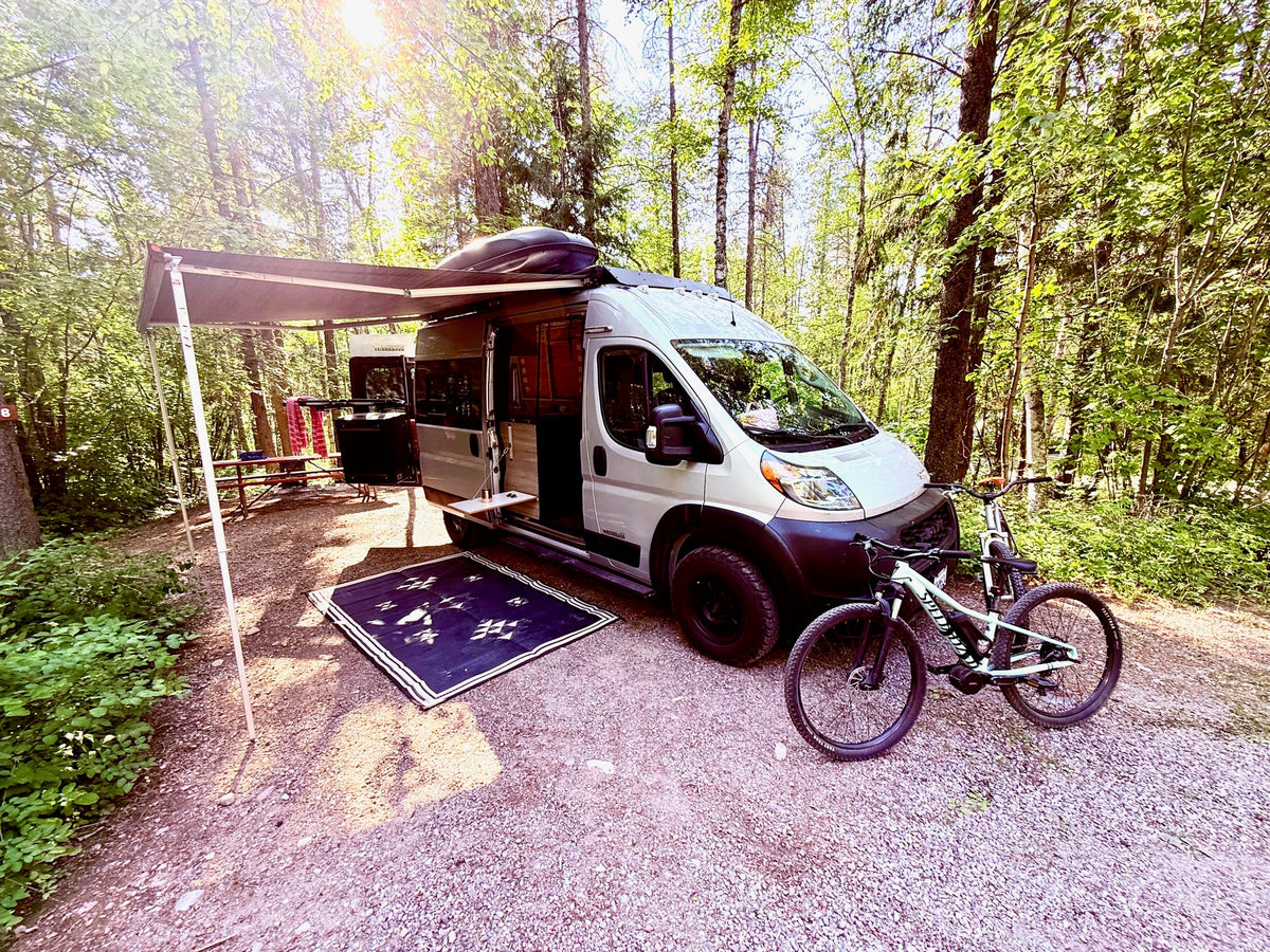 An RV rental camper van parked at a sunny forest campsite