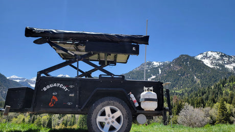 Black off-road camping trailer "Squatchy" with solar & propane, set in mountains. Ideal for an RV rental mountain escape.