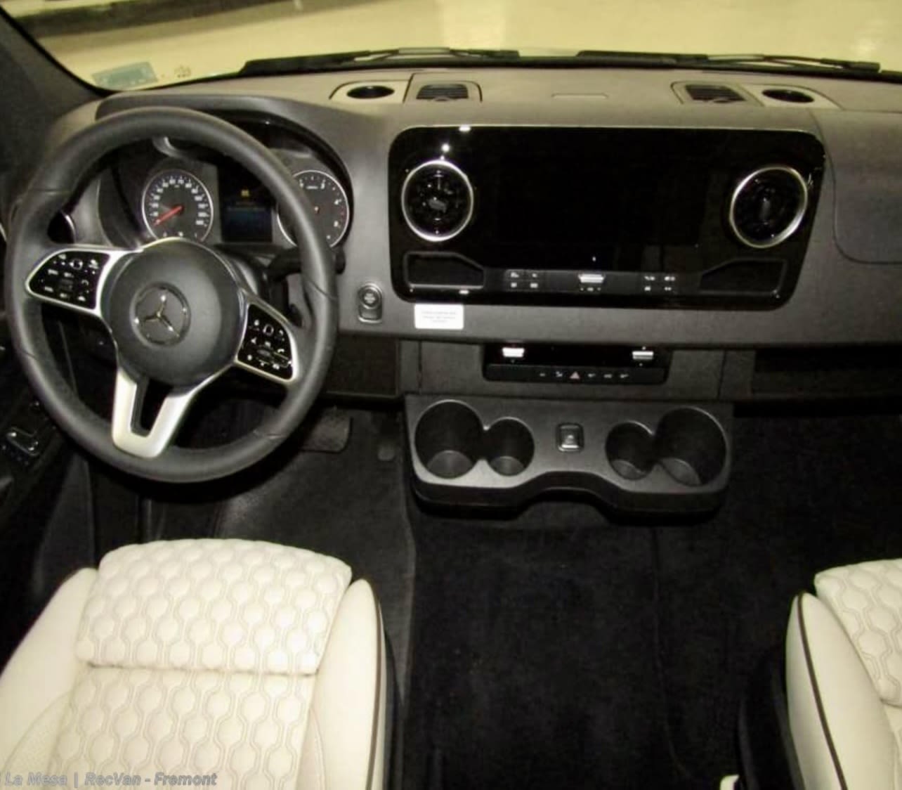 RV rental van's driver cockpit: Modern dashboard with a large screen, multi-function steering wheel, handy cup holders, and textured front seats. — photo 9