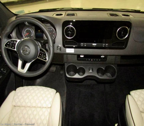 RV rental van's driver cockpit: Modern dashboard with a large screen, multi-function steering wheel, handy cup holders, and textured front seats.
