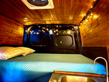 Cozy RV rental interior with warm wood paneling, string lights, a comfy bed, and a functional sink.