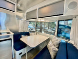 Cozy Airstream RV rental interior featuring a blue dinette, compact kitchen, and large windows with outdoor views.