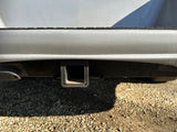 Silver RV rental's rear with trailer hitch receiver and electrical connection for towing, on gravel.