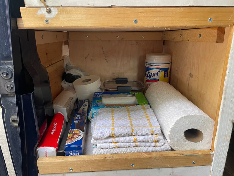  camping gear including a first aid kit on bottom shelves of a wooden cabinet.|RV rental storage under bed: A caddy with TP — photo 10