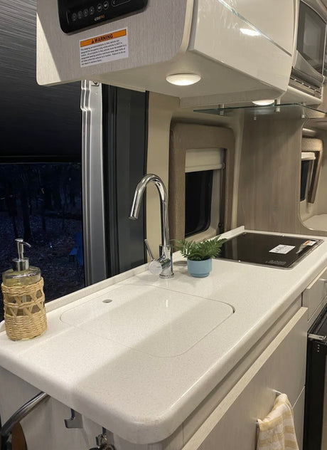 Inside a modern RV rental: sleek kitchen with sink, stovetop, & outdoor view. Compact amenities for your next adventure.