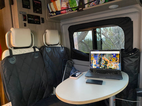 An RV rental provides a mobile office and entertainment hub, with a laptop showing a basketball game and scenic window views.