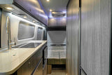 Modern rv rental interior: kitchen with sink, induction cooktop, and cozy bed area, showcasing compact luxury for travel.