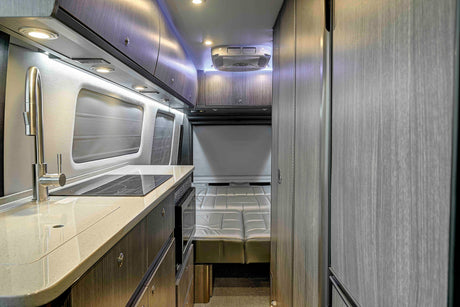 Modern rv rental interior: kitchen with sink, induction cooktop, and cozy bed area, showcasing compact luxury for travel.