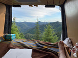 Legs propped, enjoying a breathtaking forest mountain view from the open rear of an rv rental van. Pizza & drinks present.