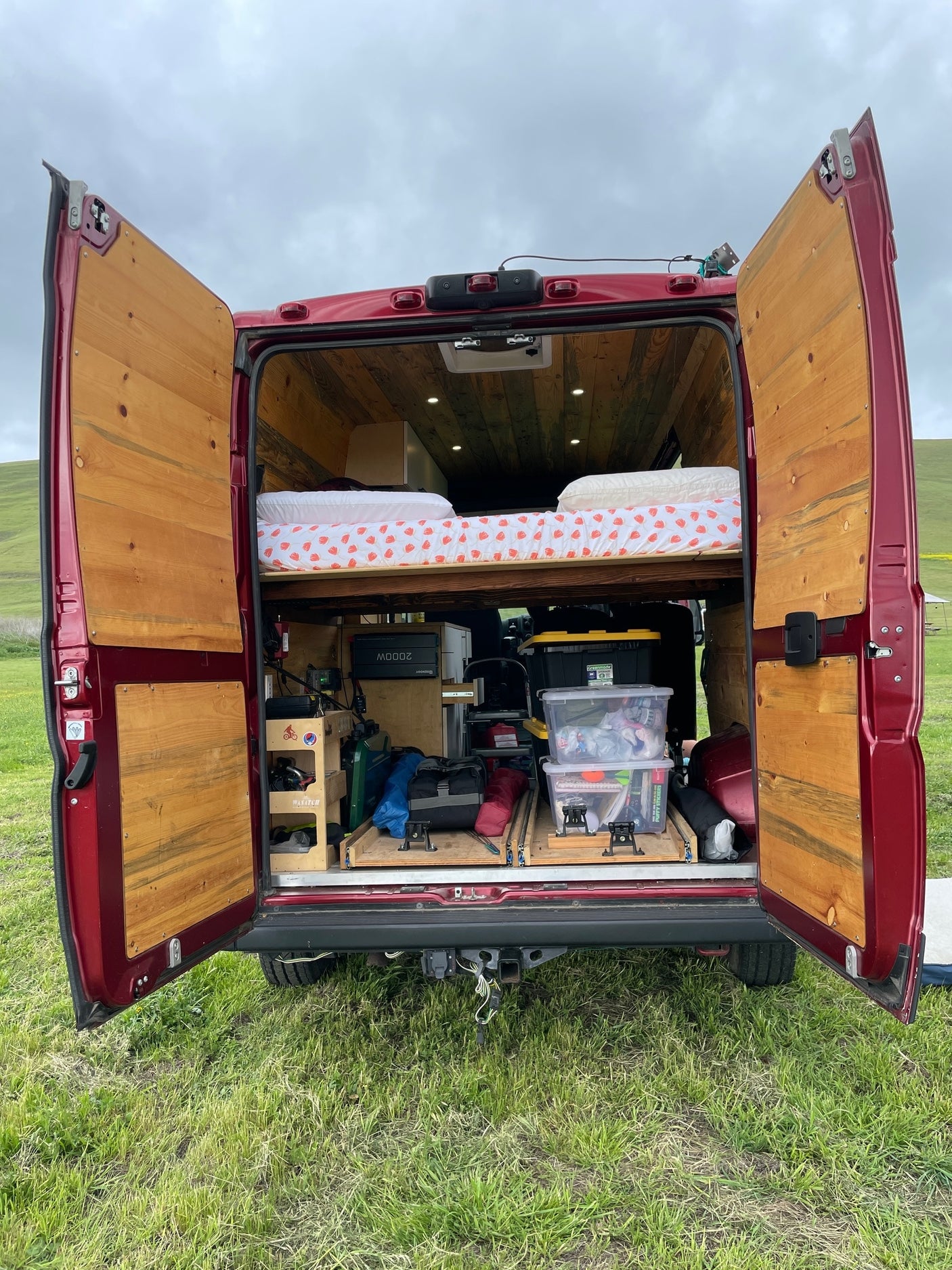 Rear view of custom red camper van, doors open, showing bed and storage. Ideal for rv rental and van life adventures in nature.