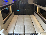 Spacious RV rental interior with a comfortable, quilted bed, dark paneling, and modern controls.