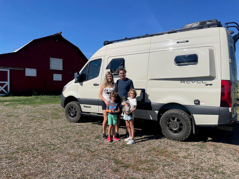 A family with two kids and a dog poses with their white Winnebago Revel RV rental in front of a red barn. — photo 6