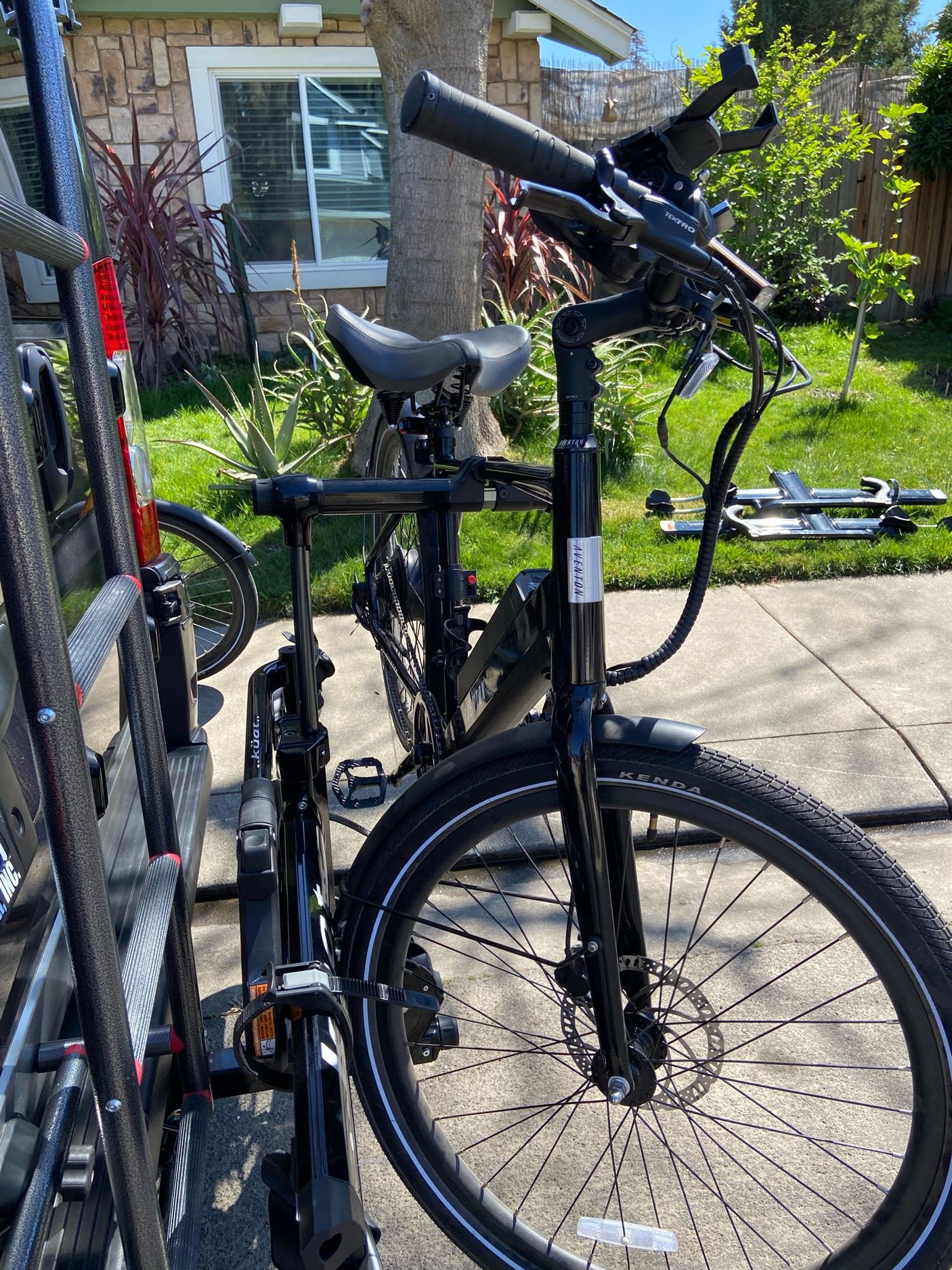 A black Aventon e-bike is securely mounted on a Kuat bike rack, attached to an rv rental vehicle for outdoor travel.
