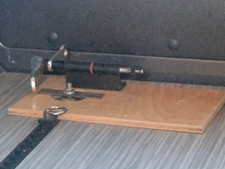 A black pen-like object is custom-mounted on a wooden base, likely for an RV rental interior, showing a clever storage solution.