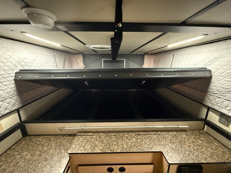 Looking up inside an RV rental pop-up camper: textured ceiling with LED lights, smoke detector, raised bed, and speckled counter.
