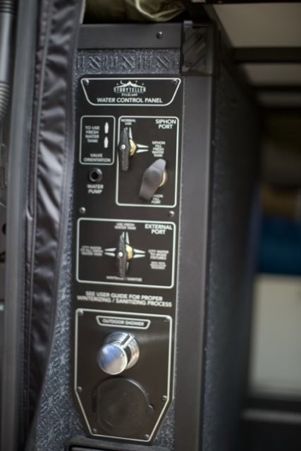  ready for your rv rental adventure.|Storyteller Overland rv rental. Rear of black camper van showing modular exterior storage with latches & stickers. Ready for adventure!|RV rental detail: Integrated utility panel with power — photo 12