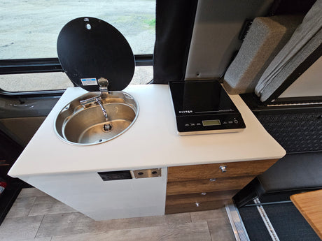 Inside this RV rental, find a compact kitchenette with a sleek induction cooktop, sink, and storage drawers. Perfect for travel.