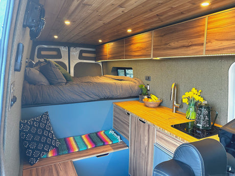 Spacious RV rental interior featuring a cozy elevated bed, modern kitchenette with wood counters, and stylish accents.