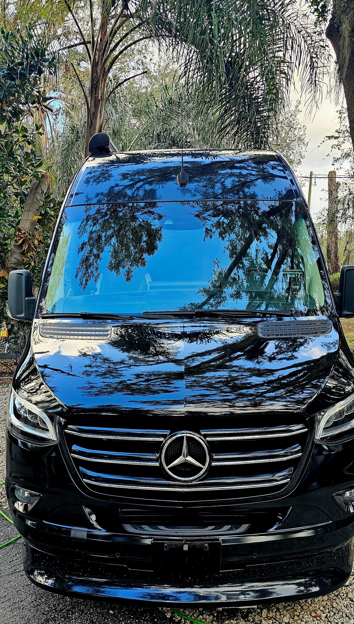 Black Mercedes-Benz Sprinter van, perfect for your next RV rental adventure. Parked outdoors with tree reflections.
