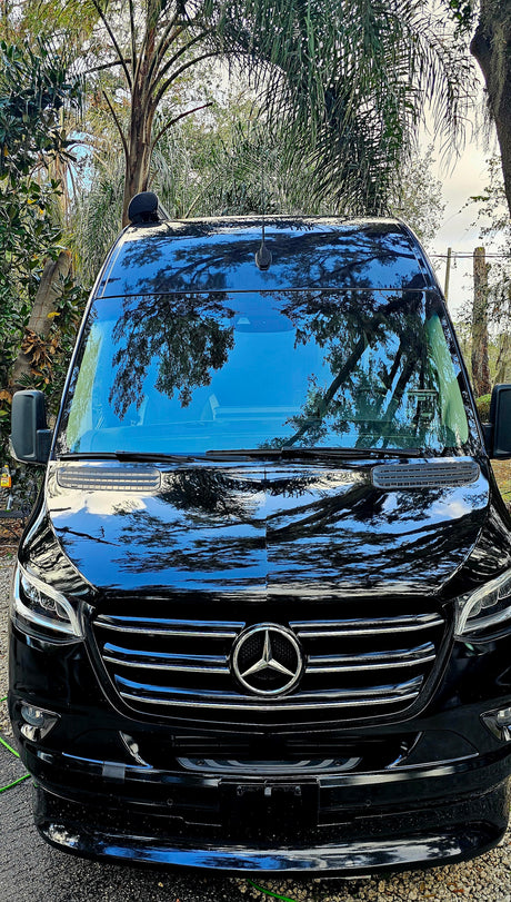 Black Mercedes-Benz Sprinter van, perfect for your next RV rental adventure. Parked outdoors with tree reflections.