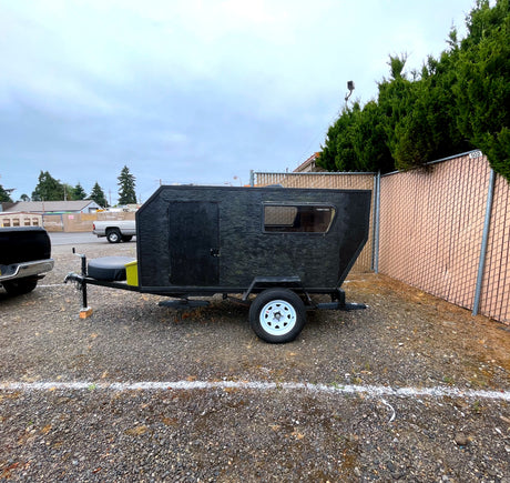 Black 'Teardrop Tom's' camper trailer on a gravel lot, an ideal RV rental for compact adventures.