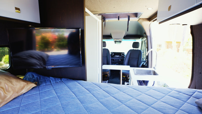 Inside a modern RV rental, featuring a comfortable bed, TV, and compact kitchen near the driver's cabin. — photo 6
