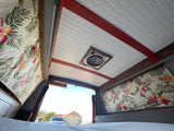 Cozy RV rental interior: tropical curtains, wood ceiling, bed, and fan visible in this custom van conversion.