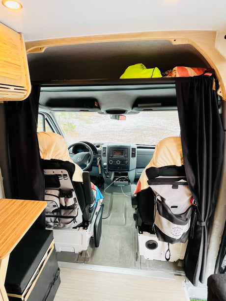 Cozy rv rental van interior looking into the driver's cabin, featuring custom storage & blackout curtains.