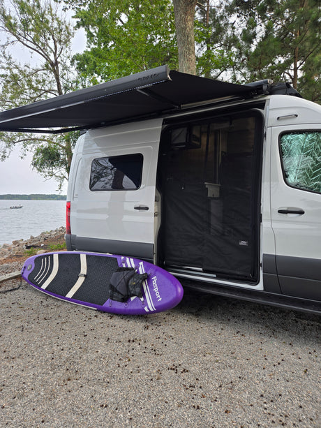 Experience an RV rental: Van life by the lake, with a paddleboard and extended awning ready for adventure.
